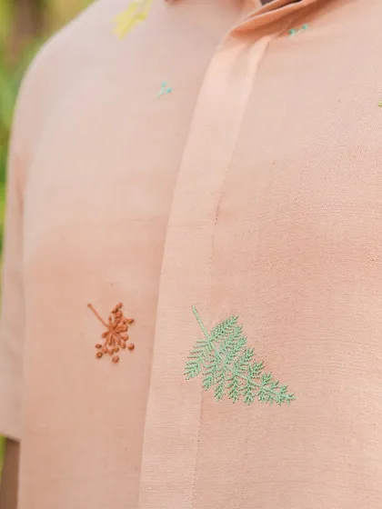 A close-up of the delicate, scattered leaf embroidery on our llama-inspired shirt. Each stitch adds to the garment's unique personality.