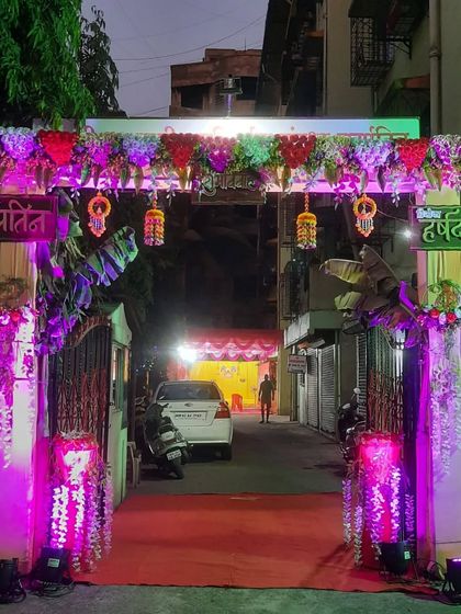 A vibrant entrance gate for a Haldi ceremony. The structure is decorated with marigolds and banana leaves, traditional elements for auspicious occasions, and lit with bright pink lights to create a festive mood right from the street.