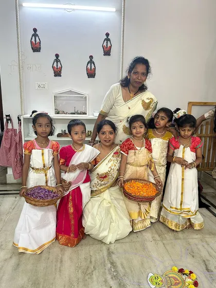 Our wonderful teachers and children dressed in traditional Onam attire, holding baskets of flowers ready for making the pookalam.