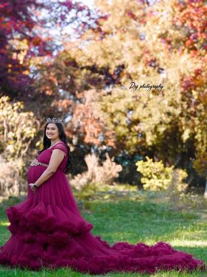 A regal portrait of a mother-to-be in a wine-colored ruffled gown and a crown, set against a beautiful autumn-colored background.