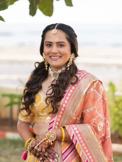 A collection from a beautiful Haldi ceremony. The bride's makeup is fresh and minimal, with a pop of color on the lips. Her hair is styled in a half-up, half-down look with braids, perfect for the fun and vibrant event.