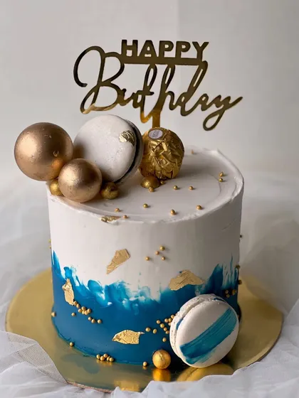 A stylish and masculine design perfect for him. This rich vanilla buttercream cake features a blue watercolor effect, gold leaf, macarons, and a Ferrero Rocher topper.
