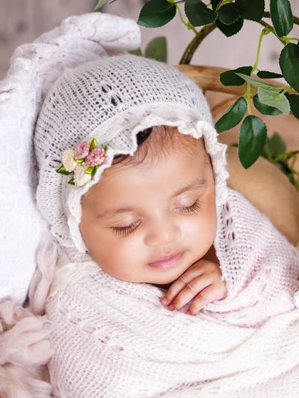 A close-up of a sleeping newborn in a delicate white bonnet, swaddled and resting in a basket. The details are just so precious.
