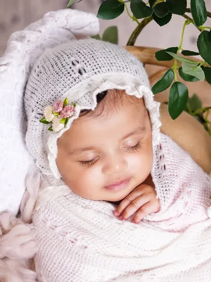 A close-up of a sleeping newborn in a delicate white bonnet, swaddled and resting in a basket. The details are just so precious.