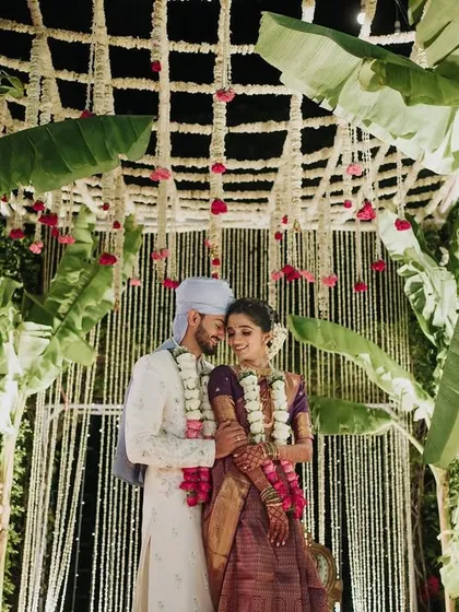 An intimate portrait of a couple under their wedding mandap. This South Indian decor features a canopy of jasmine and banana leaves, creating a beautifully traditional and fragrant setting.