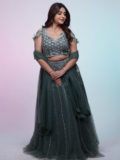 A full look at this elegant dark green lehenga. The off-shoulder feathered detail on the blouse adds a modern twist to a traditional silhouette.