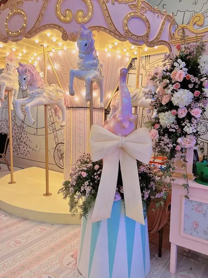 A beautiful pastel carousel with unicorns is a highlight of this whimsical princess party. The surrounding pink and white floral arrangements add to the magic.