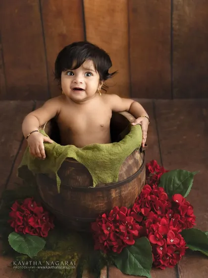 Seven-month-old Monishka peeking out of a wooden bucket with a surprised expression. These playful shots are what make sitter sessions so memorable.