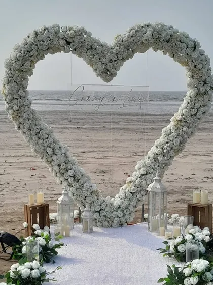 A breathtaking beach proposal setup in Mumbai, featuring a custom heart-shaped arch of white flowers and a 'Crazy in Love' neon sign. We designed this to create a truly magical and picture-perfect moment for the couple.