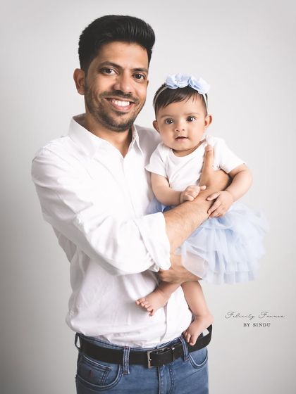 A proud father holds his adorable baby daughter in a classic studio setting. Her blue tutu adds a sweet pop of color to this simple and heartfelt portrait.