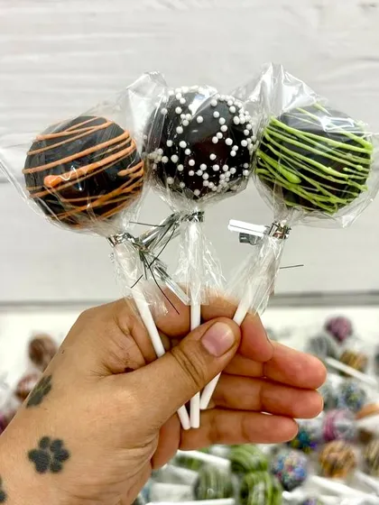 A trio of chocolate-dipped cakesicles, each with a different design: orange drizzle, white sprinkles, and green drizzle. These are perfect for party favors or adding variety to a treat box.