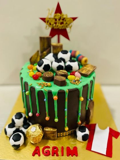 A fun and messy chocolate drip cake with a football theme, loaded with chocolates, gems, and soccer balls.