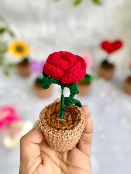 A close-up of a miniature potted red rose. Even though it's small, it has all the detail of a full-sized crochet rose.