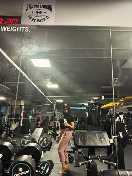 A wide shot of me in the gym. The sign in the background says "Strong enough to lift it, better be strong enough to re-rack it," a rule I live by.