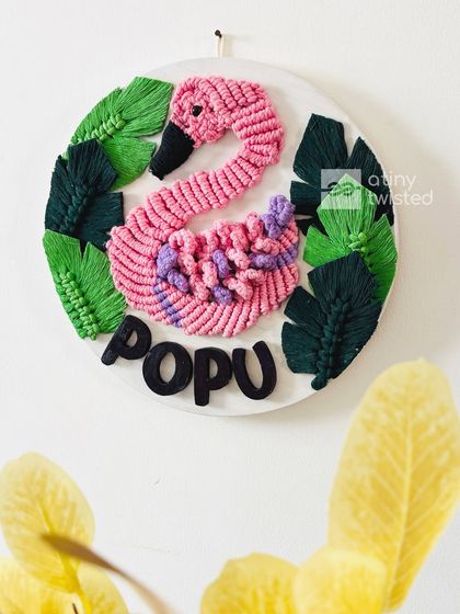 Here is another view of the custom pink and purple macramé swan nameplate for 'Popu'. The lighting highlights the texture of the knots and the contrast with the dark green macramé leaves.