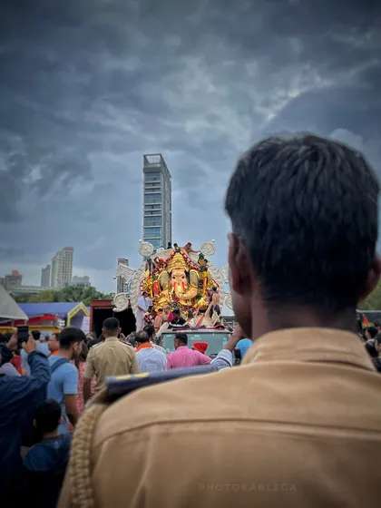 A poignant shot from behind a police officer watching over the GSB Seva Mandal Visarjan. It captures a quiet moment of duty and devotion amidst the grand scale of the event.