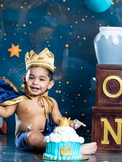 A royal first birthday! This little prince is celebrating with a crown and a cupcake in a space-themed setting.