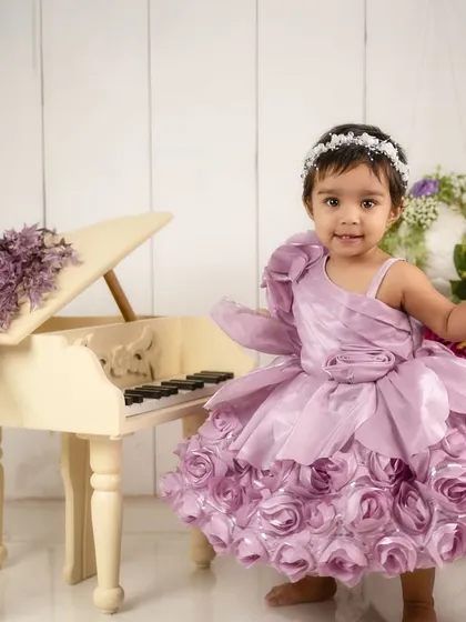 A little musician in the making. This one-year-old looks adorable in her floral purple dress next to the miniature piano.