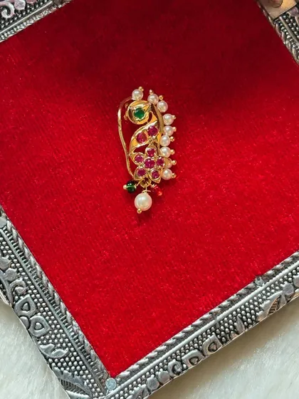 A colourful Nath with red and green stones, perfect for matching with a bridal saree. The design is intricate and traditional.