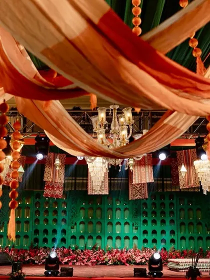 A vibrant Moroccan-themed stage with a teal backdrop, red flooring, and a ceiling of draped fabrics and hanging rugs, creating a rich and layered look.