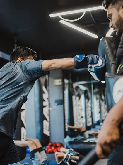 A student practices his straight right on the focus mitts, aiming for precision and power under the coach's guidance.