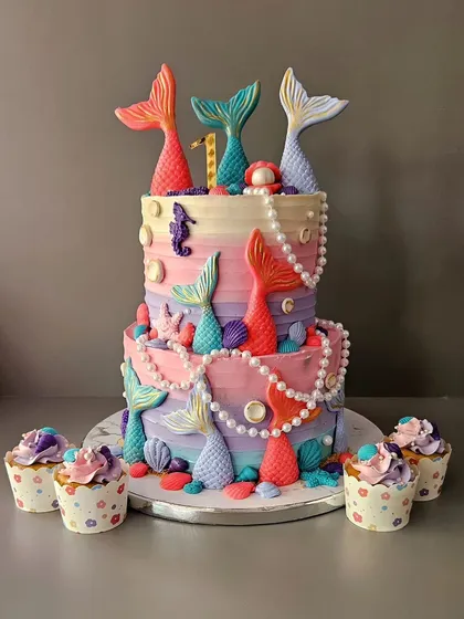 This two-tier mermaid cake was a dream to make for a first birthday party. It features multiple mermaid tails, edible pearls, and seashells in a beautiful pastel palette. I also made matching cupcakes to complete the underwater treasure theme.