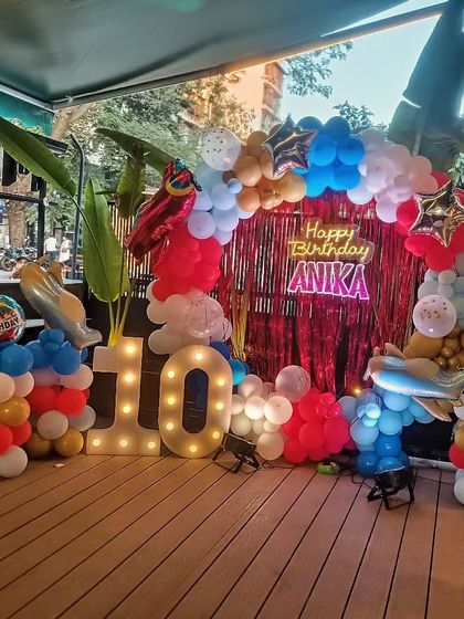 An airplane theme ready for takeoff! This outdoor deck setup for a 10th birthday features a balloon arch with airplane foil balloons, a red fringe backdrop, and a light-up marquee number.