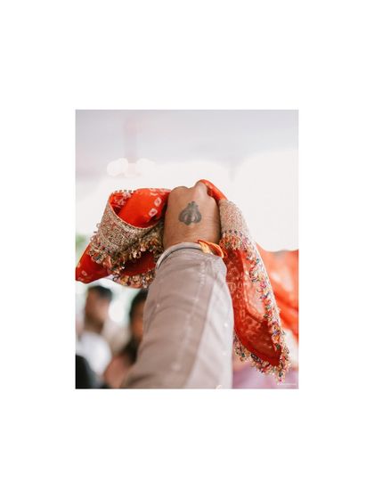 A detail shot focusing on a hand holding a traditional red cloth. The shallow depth of field and the symbolic spade tattoo create a simple yet powerful image.