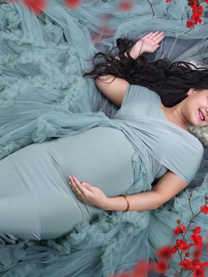 An artistic overhead shot of the mom-to-be resting. The soft green fabric and the frame of red flowers create a striking and beautiful color contrast.
