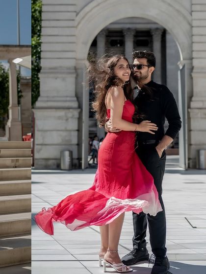 A playful moment captured in the London breeze. The wind catches the bride's dress as she shares a laugh with her partner, creating a dynamic and joyful image.