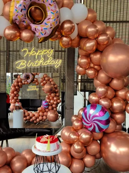 A close-up of the fun details in this rose gold birthday setup, including a donut and candy foil balloon, a neon sign, and a custom cake.