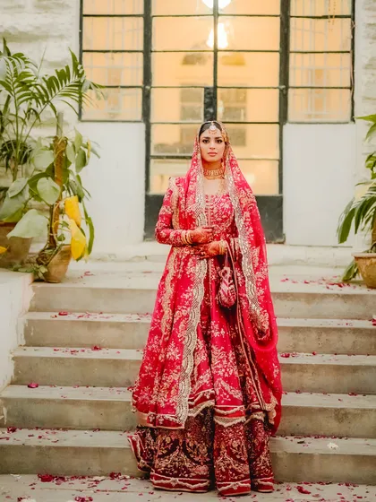 Here is a bride embodying pure grace and elegance on her Nikah day. Her magnificent red lehenga stands out against the timeless stone architecture, creating a portrait that is both regal and deeply personal. I believe in capturing the bride's individual story and presence in a way that feels majestic.