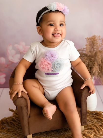 A baby girl sticks her tongue out playfully while sitting in a miniature armchair.