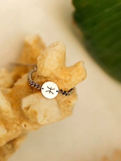 A product shot of the silver Pisces zodiac bracelet resting on a piece of coral, giving it a natural, beach-inspired feel.