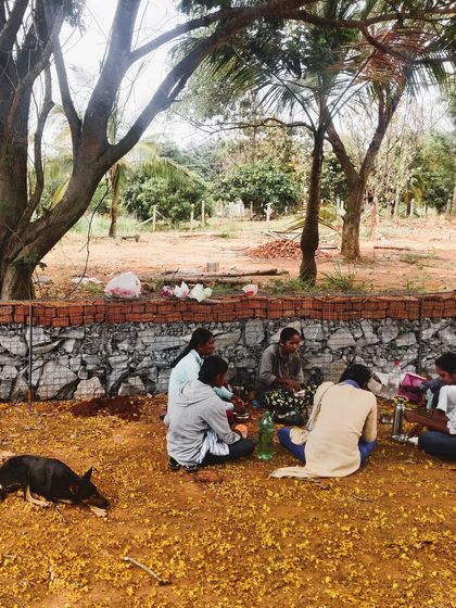 A well-deserved break. The team, including a furry site supervisor, enjoys a moment of rest and community against the backdrop of the gabion wall they built together.