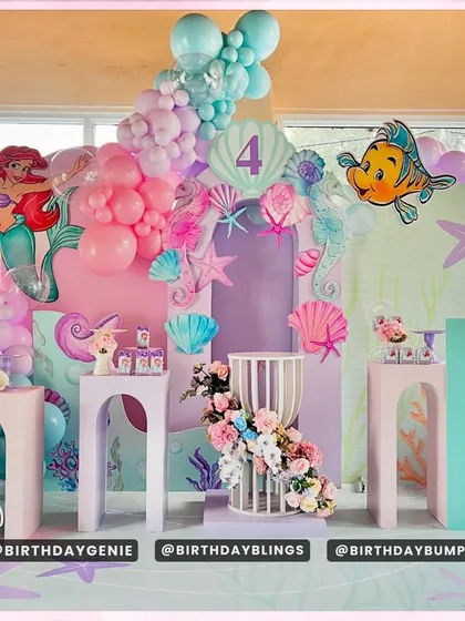 A magnificent Little Mermaid party with a multi-layered, underwater castle-like backdrop. The scene is filled with characters like Ariel, Flounder, and Sebastian, and decorated with pastel balloons and floral arrangements.