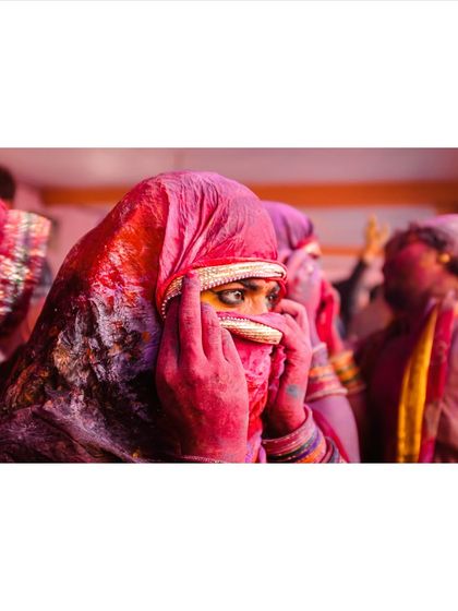A woman peeks out from behind her red veil during Holi celebrations. Her eyes, full of emotion, are the focal point of this intimate and colorful portrait.
