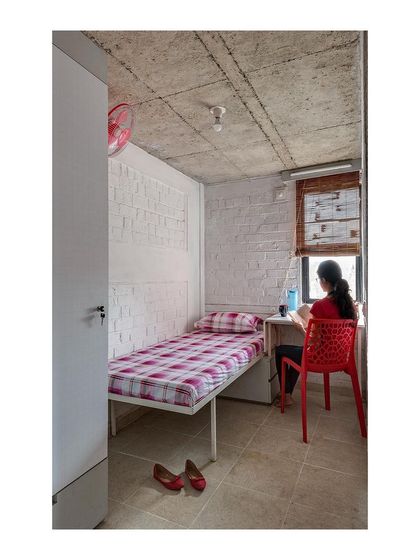 The personal study and sleeping area in the student housing unit. The design utilizes a pared-down material palette of whitewashed brick and bare concrete, creating a durable and minimalist backdrop for student life.