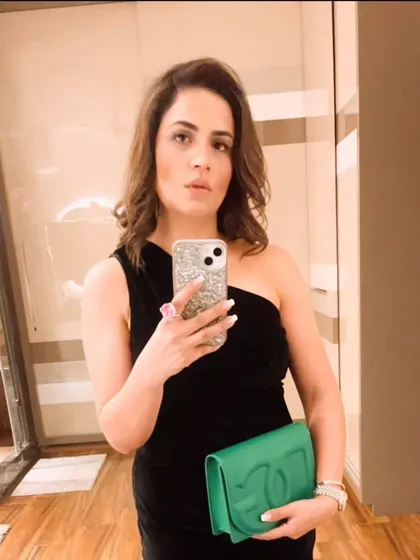 A close-up mirror selfie showing the details of this classic black dress look. The one-shoulder neckline, sparkling phone case, and a statement pink ring come together to create a chic and personalized party outfit.