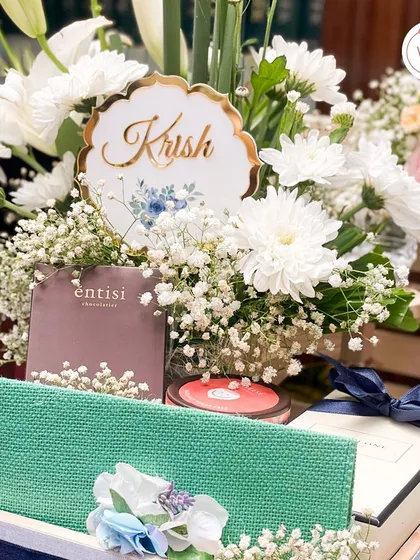 A personalized hamper for "Krish," filled with curated gifts from Jo Malone and Entisi, surrounded by a lush bed of fresh white flowers. It shows how we tailor each gift to the individual.