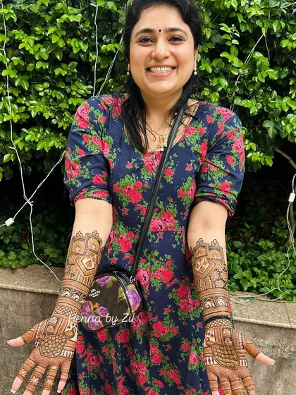 A happy client showing off her full-arm traditional mehendi, filled with elephants, peacocks, and jharokhas.