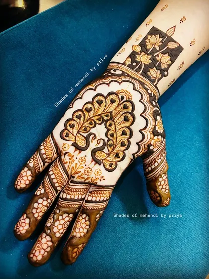 I love using negative space to make the main figures stand out. Here, a heart-shaped peacock design on the back of the hand is complemented by a bold lotus pattern on the wrist, creating a modern yet traditional feel.