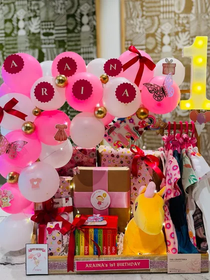 The full view of Araina's first birthday hamper, a grand arrangement in pink with personalized balloons, a light-up number '1', and a mini wardrobe of dresses.