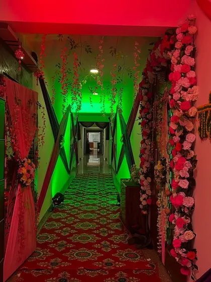 A hallway decorated with a floral arch and green lighting, leading to the main event area.