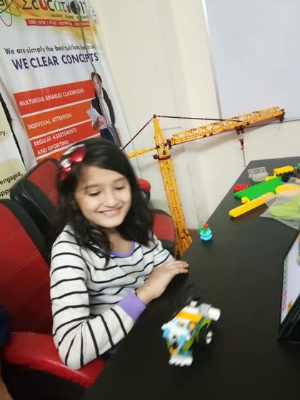 A girl smiles as she tests the program for her small, wheeled robot in our classroom.