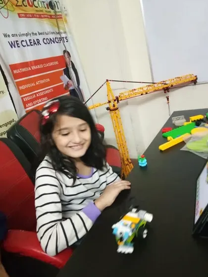 A girl smiles as she tests the program for her small, wheeled robot in our classroom.