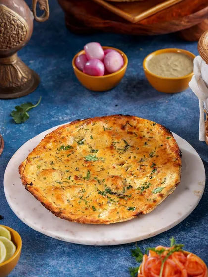 A perfectly cooked Garlic Naan on a marble platter. The lighting is focused on capturing the golden-brown blisters and fresh garlic, making the bread look irresistibly crisp and flavorful.