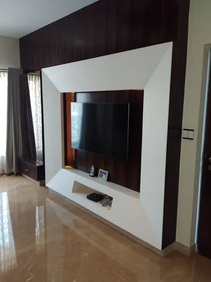 This living room features a bold and sculptural TV unit that serves as the room's focal point. The television is framed by a massive, bevelled white structure set against a dark wood panelled wall, creating a powerful visual contrast and a high-impact entertainment zone.