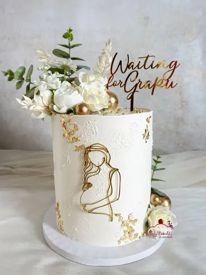 An elegant and modern cake to celebrate a new beginning. This tall baby shower cake features a clean white buttercream finish, delicate gold leaf, fresh eucalyptus, and a beautiful line-art topper.