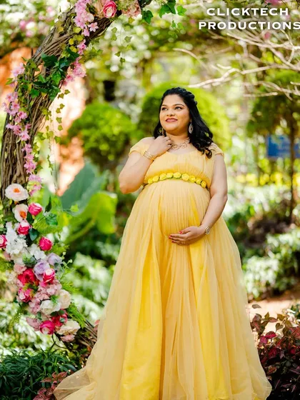 A solo maternity portrait in a yellow gown, framed by a rustic floral arch.